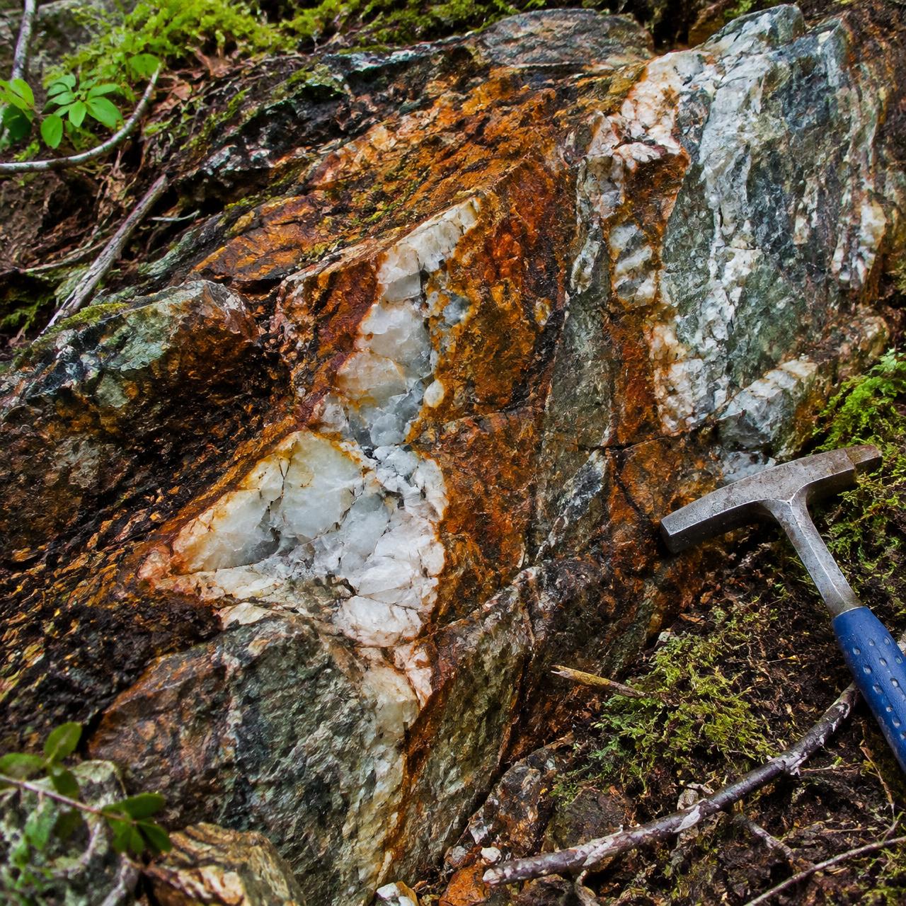 Iron-stained quartz vein outcrop with a geological hammer